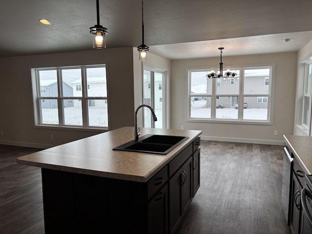 kitchen featuring sink, a center island with sink, dark hardwood / wood-style floors, pendant lighting, and stove