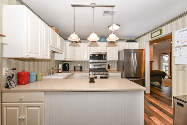 kitchen with visible vents, a peninsula, stainless steel appliances, light countertops, and a sink