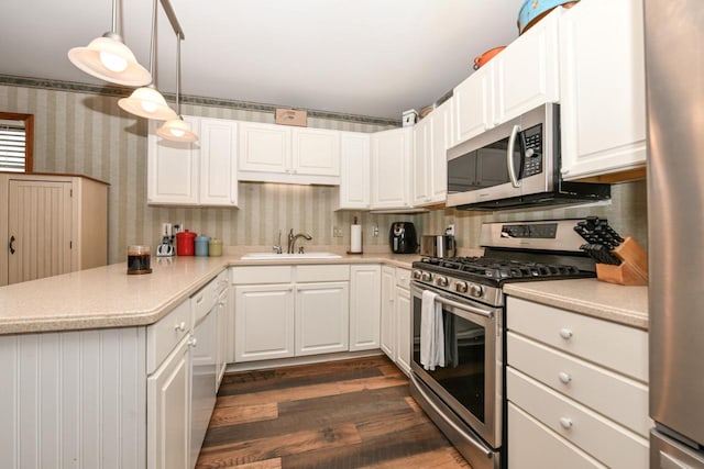 kitchen with light countertops, appliances with stainless steel finishes, a sink, a peninsula, and wallpapered walls