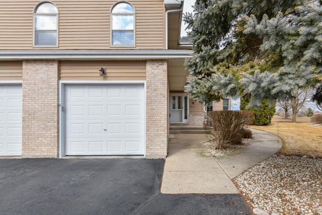 view of front of home featuring driveway, a garage, and brick siding