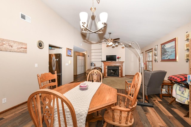 dining space with ceiling fan with notable chandelier, dark wood-style flooring, a brick fireplace, and visible vents