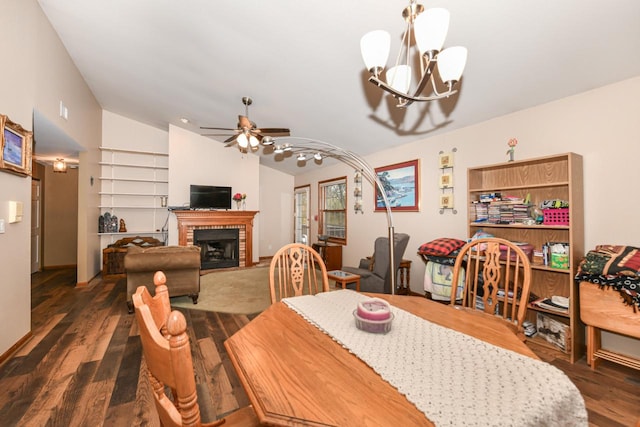 dining room with lofted ceiling, ceiling fan with notable chandelier, a brick fireplace, and wood finished floors