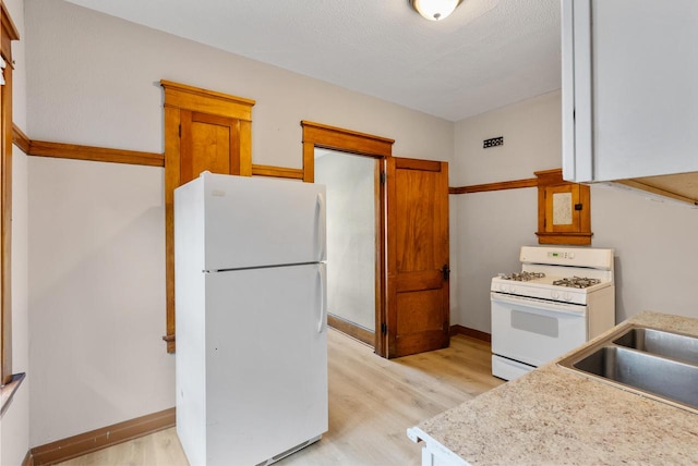 kitchen featuring sink, white appliances, a textured ceiling, and light hardwood / wood-style flooring