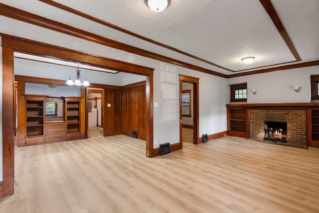 unfurnished living room featuring a brick fireplace, an inviting chandelier, crown molding, a textured ceiling, and light wood-type flooring