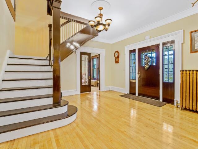 foyer entrance with radiator heating unit, wood-type flooring, a notable chandelier, and ornamental molding