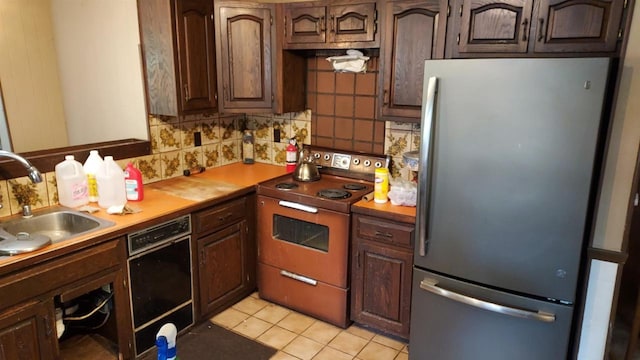 kitchen with stove, sink, stainless steel fridge, light tile patterned floors, and dark brown cabinets