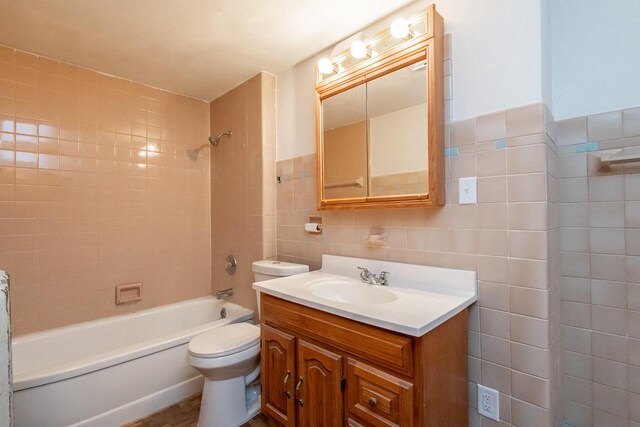 full bathroom with tiled shower / bath, vanity, toilet, and tile walls