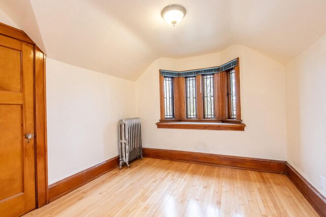 additional living space with radiator, light hardwood / wood-style flooring, and lofted ceiling