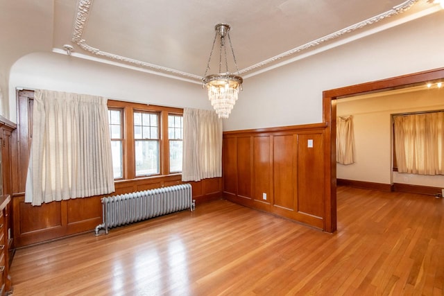 spare room featuring radiator, wooden walls, light hardwood / wood-style flooring, and an inviting chandelier