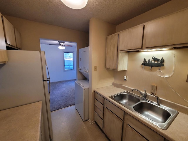 kitchen featuring white refrigerator, sink, ceiling fan, a textured ceiling, and stacked washer / drying machine