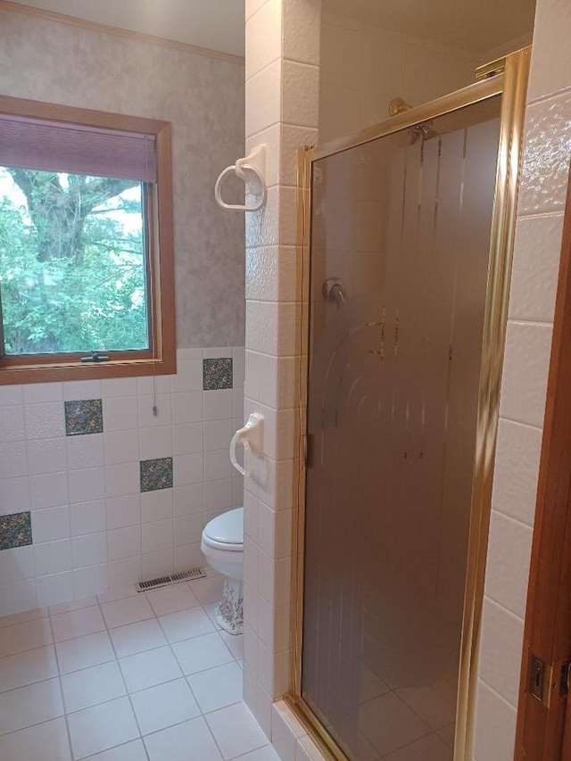 bathroom with tile patterned flooring, toilet, a shower with door, and tile walls