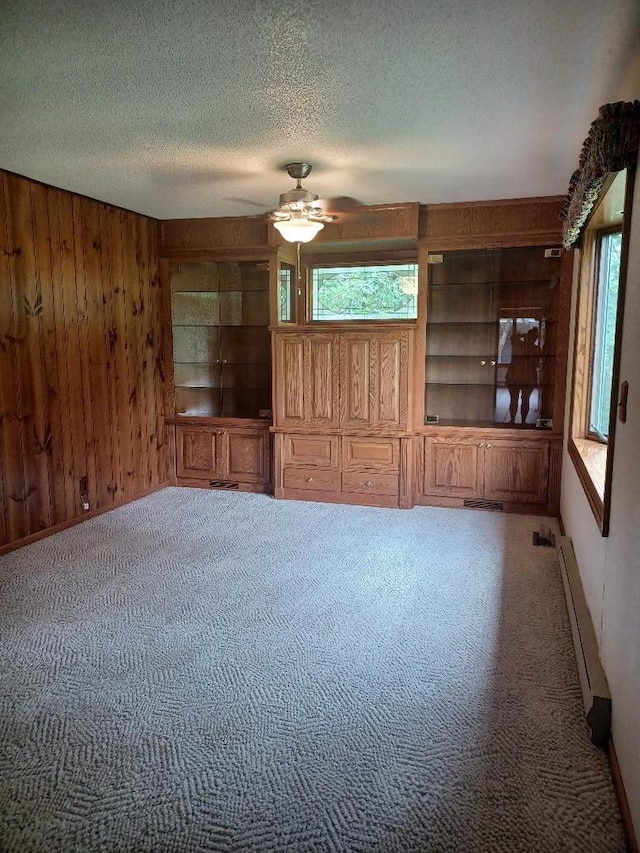 unfurnished living room featuring carpet floors, wood walls, and ceiling fan