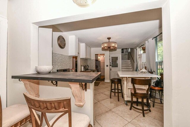 kitchen featuring white cabinets, a kitchen breakfast bar, decorative backsplash, light tile patterned floors, and kitchen peninsula