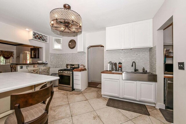 kitchen featuring gas range, light tile patterned floors, sink, and white cabinets