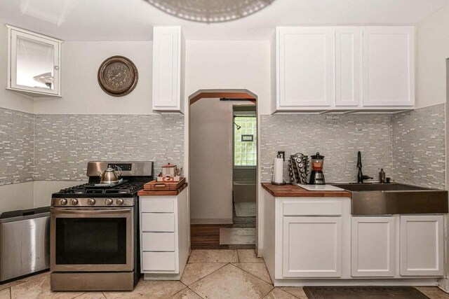 kitchen with butcher block counters, sink, gas stove, tasteful backsplash, and white cabinets