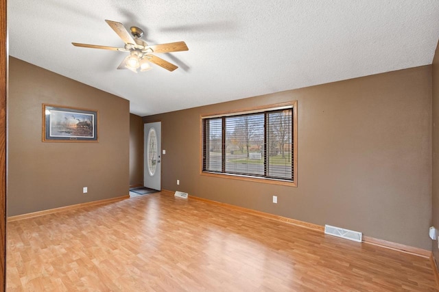 empty room featuring ceiling fan, lofted ceiling, a textured ceiling, and light hardwood / wood-style flooring