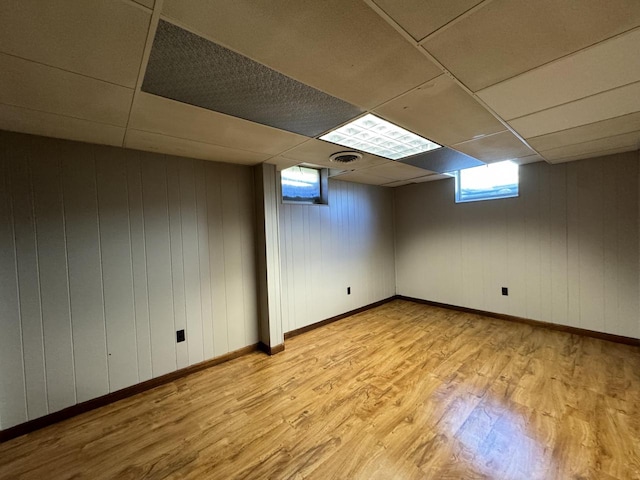 basement with light hardwood / wood-style flooring, a drop ceiling, and wooden walls