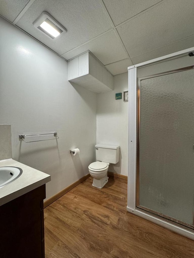 bathroom with a drop ceiling, hardwood / wood-style floors, toilet, vanity, and a shower with shower door