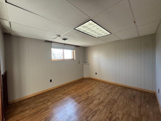 basement featuring wood-type flooring, a paneled ceiling, and wood walls