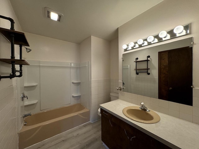 full bathroom featuring wood-type flooring,  shower combination, toilet, vanity, and tile walls