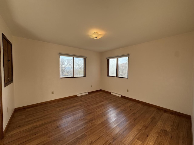 spare room featuring baseboard heating and dark hardwood / wood-style flooring