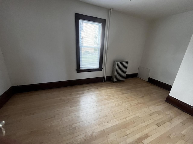 unfurnished room featuring radiator heating unit and light hardwood / wood-style flooring