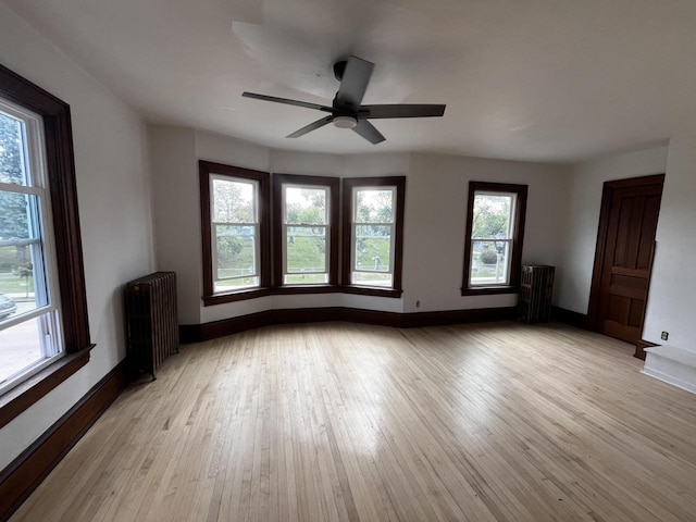 spare room featuring ceiling fan, radiator heating unit, and light wood-type flooring