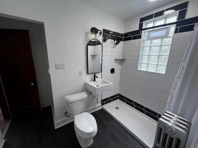 bathroom featuring a tile shower, sink, wood-type flooring, radiator heating unit, and toilet