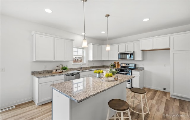 kitchen with light wood-type flooring, appliances with stainless steel finishes, a center island, and white cabinetry