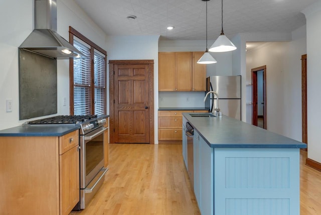 kitchen featuring a center island with sink, wall chimney range hood, sink, hanging light fixtures, and appliances with stainless steel finishes