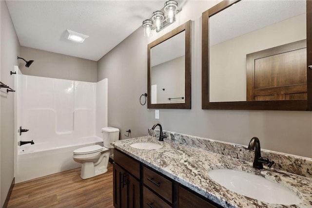 full bathroom featuring wood-type flooring, a textured ceiling, toilet, vanity, and shower / bathtub combination