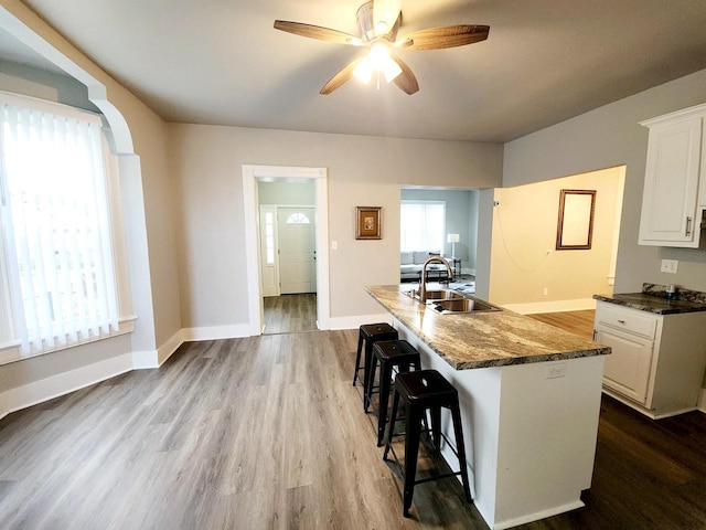 kitchen with a kitchen bar, ceiling fan, sink, light hardwood / wood-style flooring, and white cabinetry