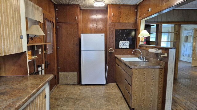 33135 Fulton St, Lone Rock, WI 53556 - kitchen featuring freestanding refrigerator, a sink, wooden walls, brown cabinetry, and dark countertops