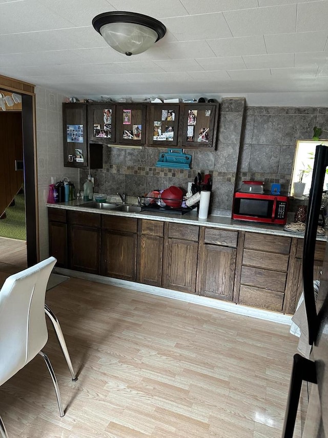 bar featuring tile walls, dark brown cabinetry, sink, and light hardwood / wood-style flooring