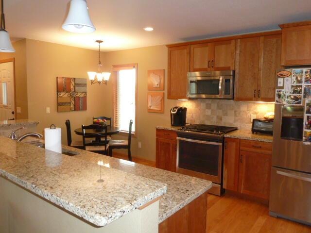 kitchen with light stone countertops, light hardwood / wood-style flooring, pendant lighting, and appliances with stainless steel finishes