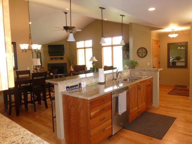 kitchen featuring light hardwood / wood-style flooring, stainless steel dishwasher, hanging light fixtures, and lofted ceiling