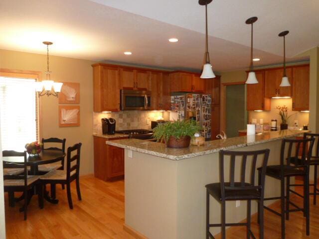 kitchen with kitchen peninsula, light stone counters, stainless steel appliances, light hardwood / wood-style floors, and hanging light fixtures