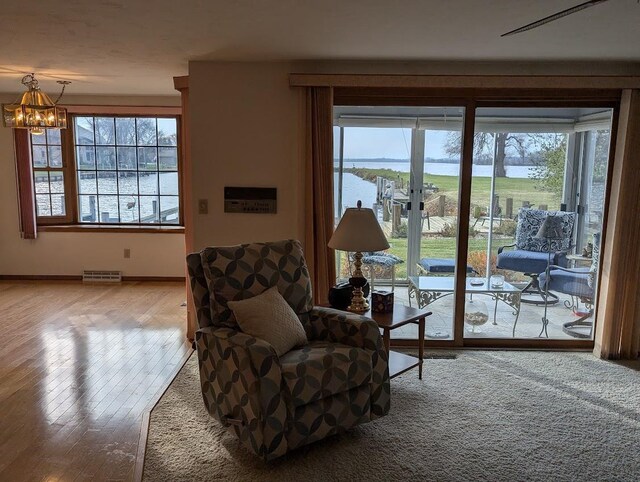 living area featuring hardwood / wood-style floors, plenty of natural light, a water view, and a chandelier