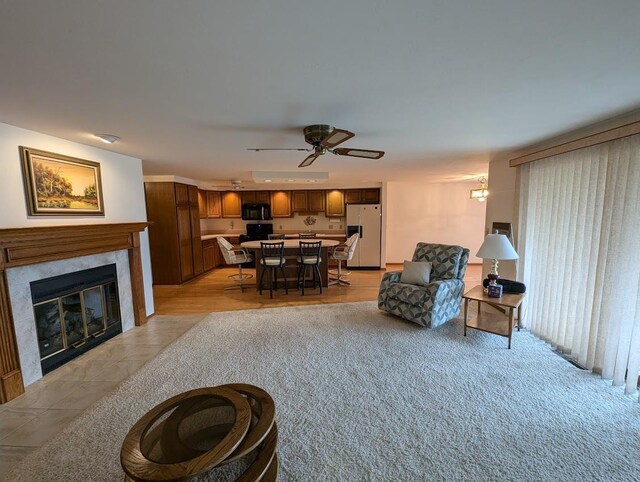 living room with a tile fireplace, light wood-type flooring, and ceiling fan