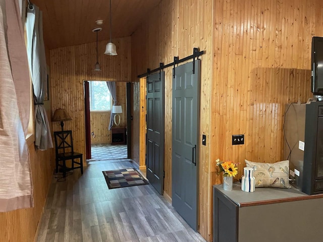 hall featuring dark hardwood / wood-style floors, a barn door, a towering ceiling, and wooden walls