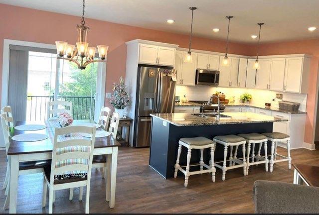 kitchen with white cabinets, appliances with stainless steel finishes, decorative light fixtures, and an island with sink