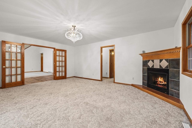 unfurnished living room with a tile fireplace, french doors, carpet, and a chandelier