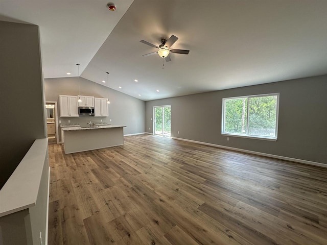 unfurnished living room with ceiling fan, sink, vaulted ceiling, and light wood-type flooring