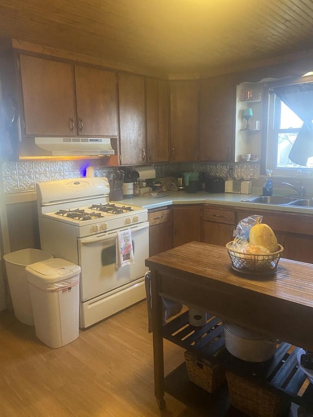 kitchen with decorative backsplash, white gas stove, light hardwood / wood-style floors, and sink