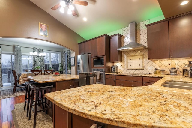 kitchen featuring wall chimney exhaust hood, hanging light fixtures, stainless steel appliances, lofted ceiling, and a breakfast bar area