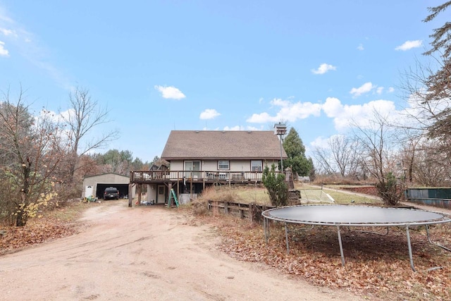 view of front of home with a trampoline, a garage, an outdoor structure, and a wooden deck