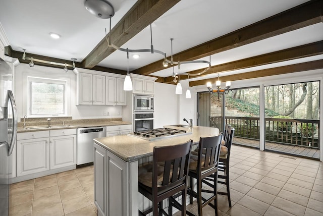 kitchen with stainless steel appliances, beam ceiling, decorative light fixtures, a center island with sink, and white cabinetry