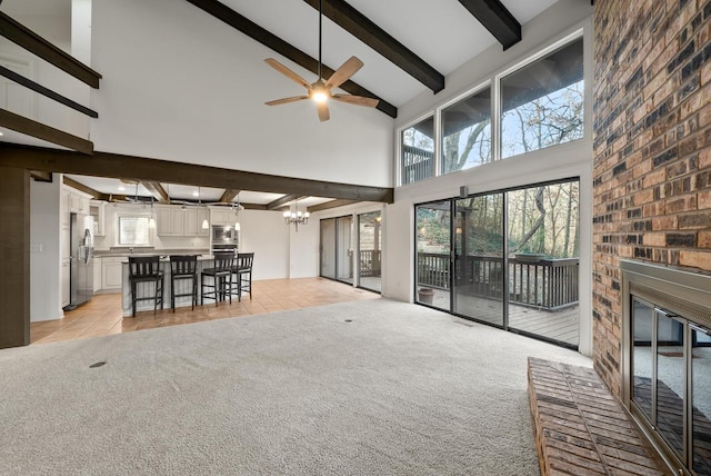 unfurnished living room with beam ceiling, a brick fireplace, high vaulted ceiling, light carpet, and ceiling fan with notable chandelier