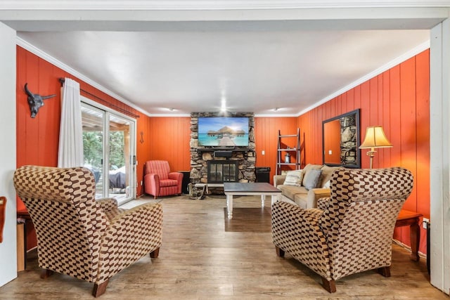 living room featuring wood walls, wood-type flooring, ornamental molding, and a fireplace