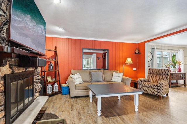 living room with crown molding, a fireplace, wooden walls, and light wood-type flooring